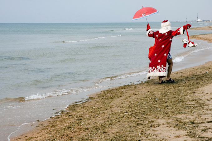 Дед Мороз бегает с зонтиком по морскому пляжу. Фото: Ольга Василькова/Коммерсантъ